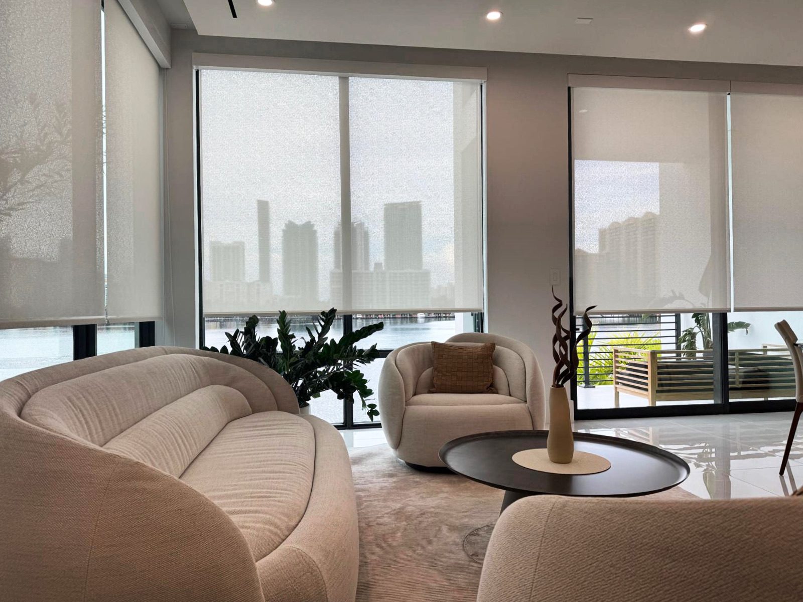 Solar roller shades lowered across floor to ceiling windows in a Miami high-rise with the bay and skyline beyond
