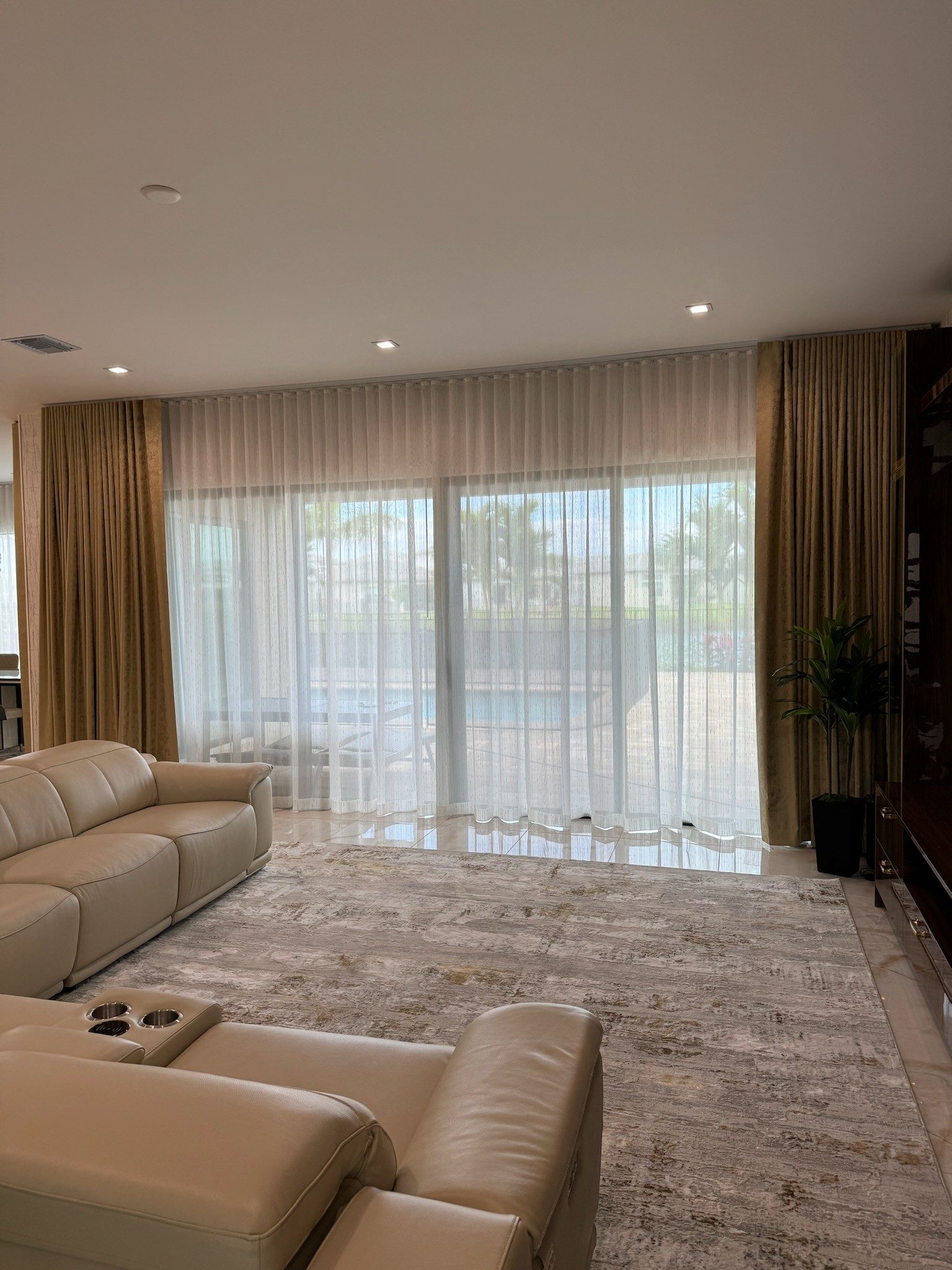 Sheers layered inside gold drapery panels across a pool-facing slider, breaking slightly at the floor.