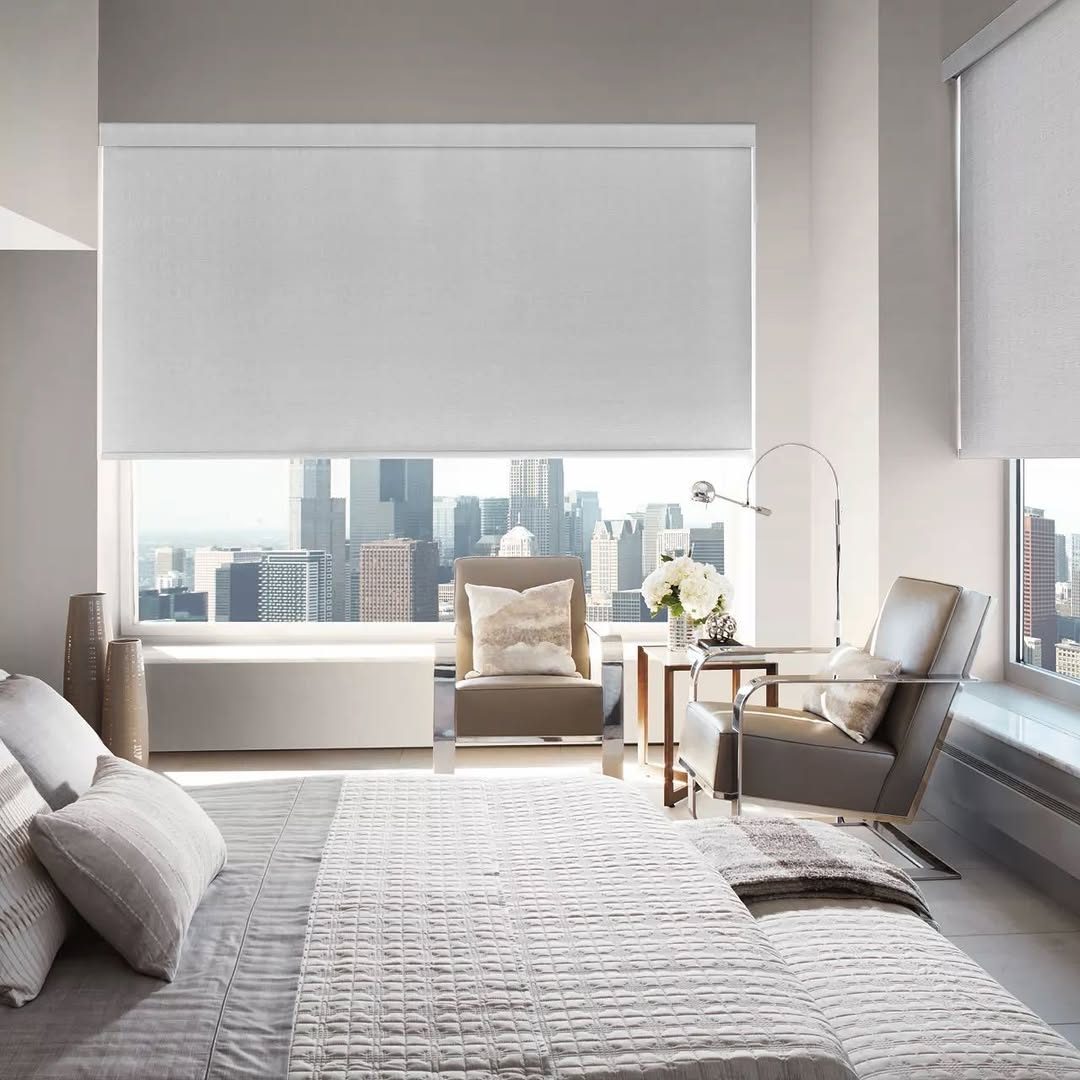 A blackout roller shade over a bedroom window, the city still bright beyond the edge of the cloth.