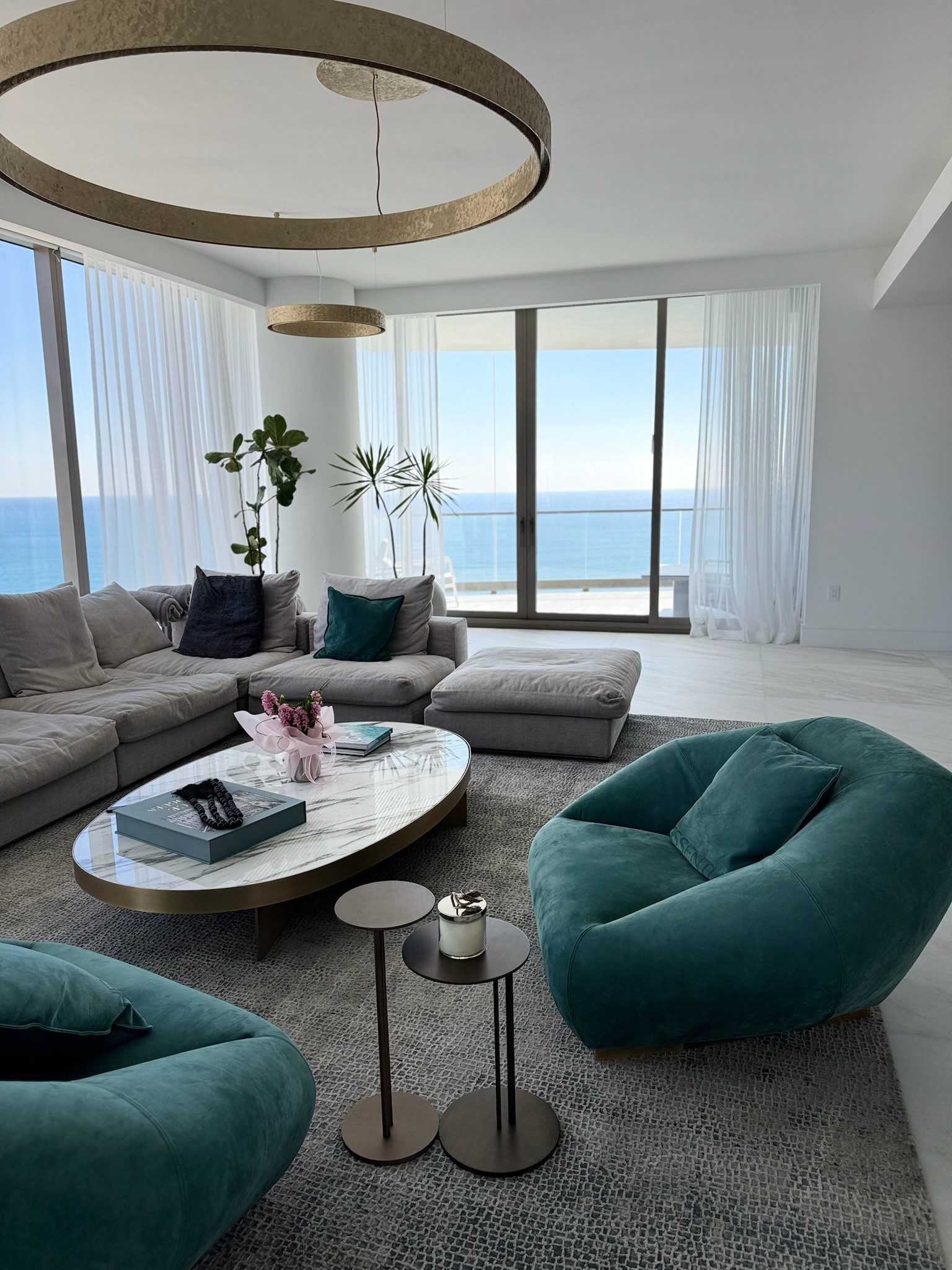 White sheer panels running the full height of an oceanfront living room, stacked clear of the glass.