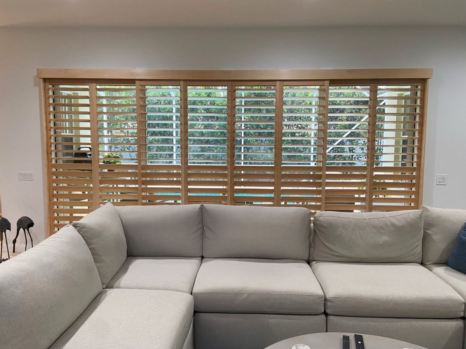Light wood plantation shutters spanning a wide window behind a sectional sofa
