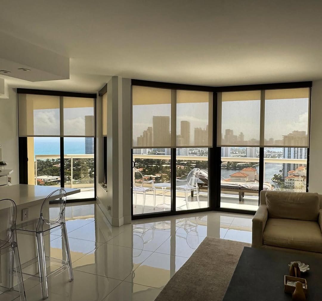 Cream solar shades part-drawn on a corner unit, holding the ocean and skyline while taking the heat off the glass.