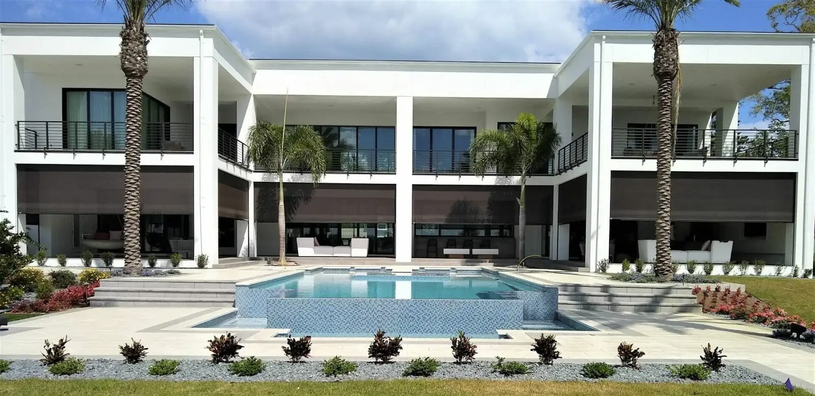 Motorized outdoor screens lowered across the covered terraces of a modern waterfront home