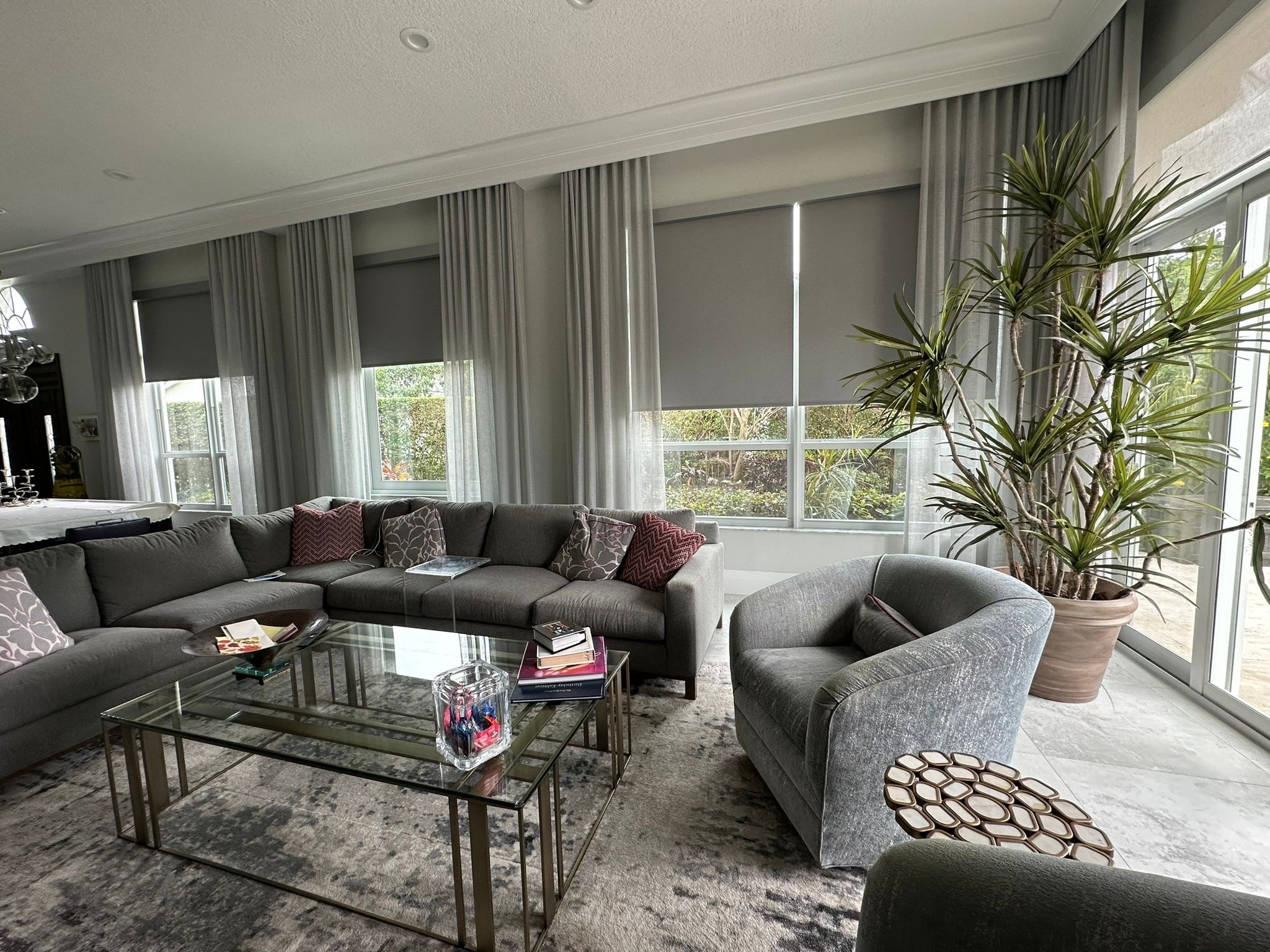 Grey roller shades layered with sheer drapery across a living room wall.