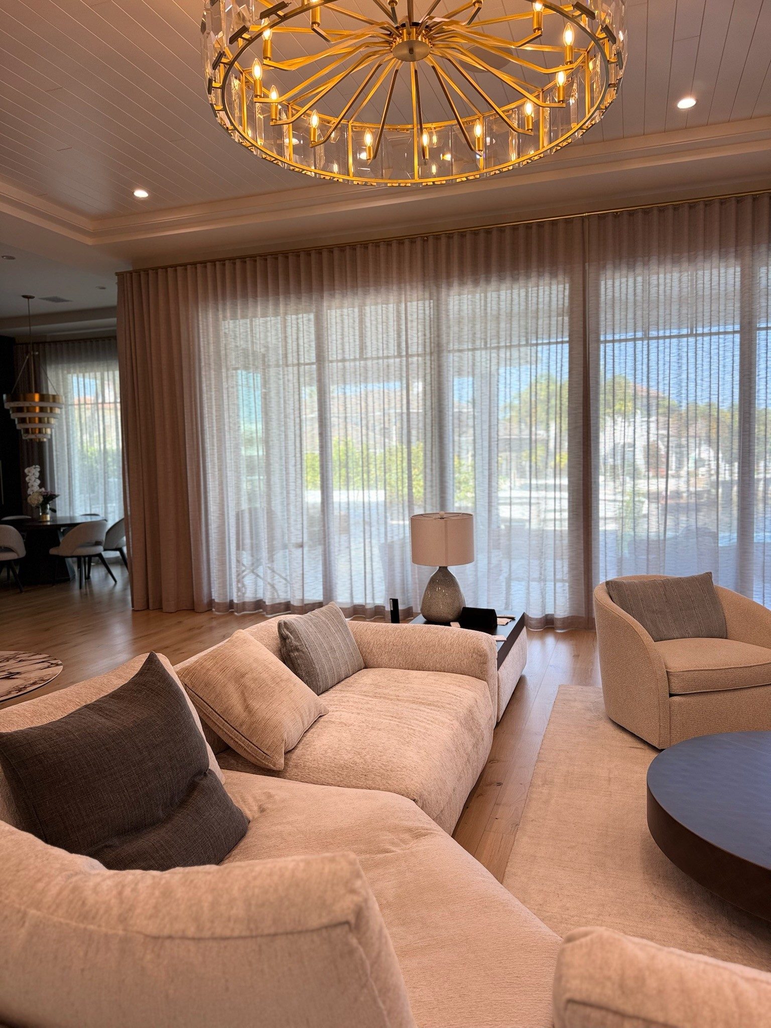 Sheers on a concealed track with blush side panels, under a gold chandelier, facing the water.