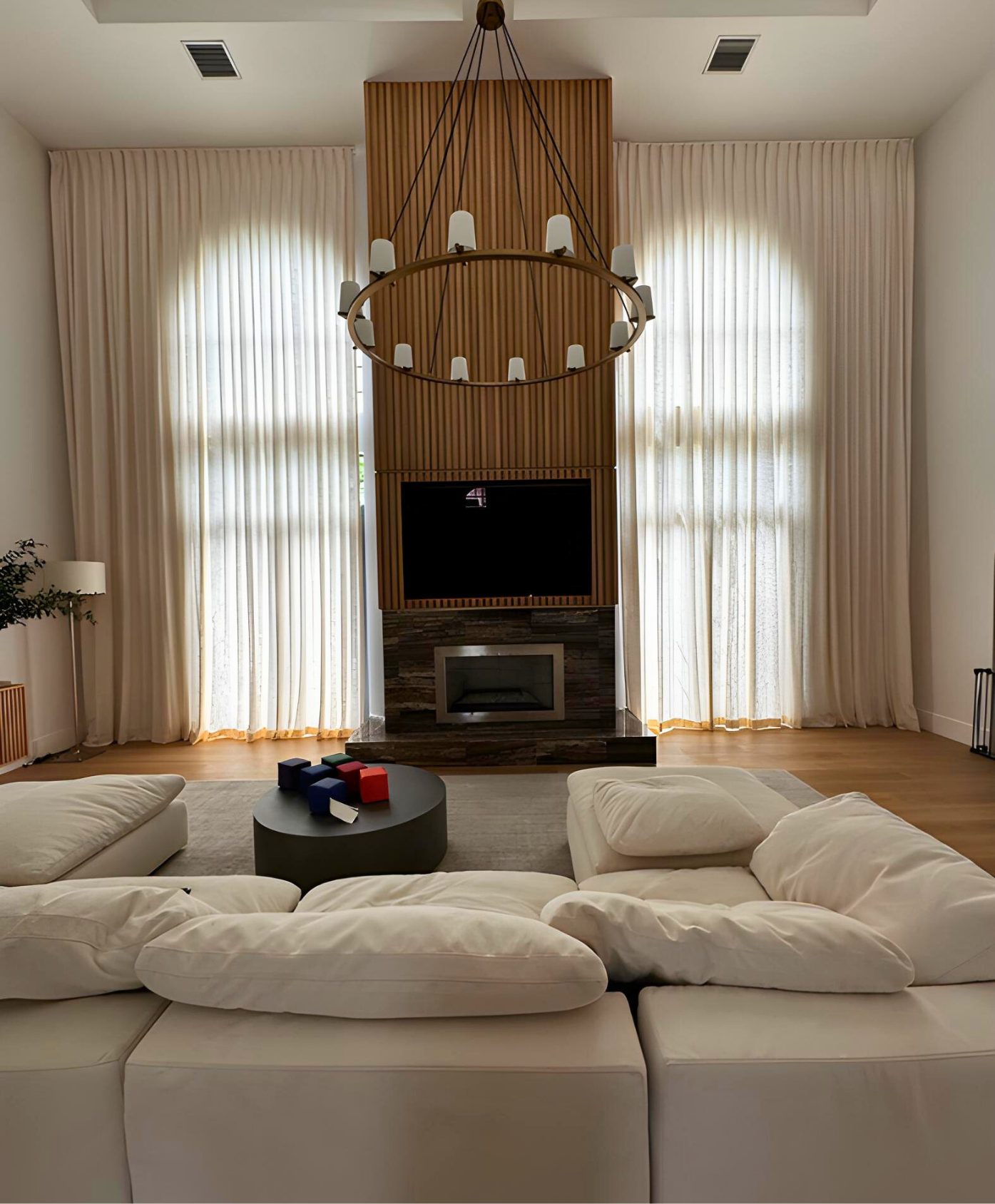 Ivory drapery running two storeys either side of a slatted wood fireplace wall in a double-height room.