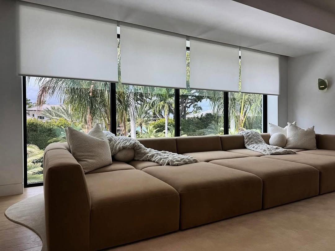 White roller shades held at half drop over sliding doors, cutting the low sun off the seating without closing out the garden.