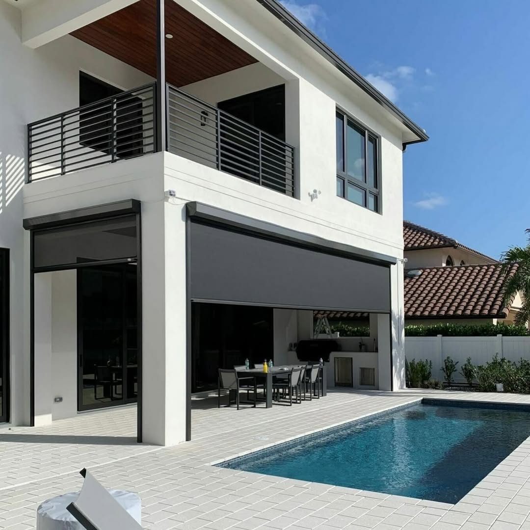 A dark solar screen closing off a poolside summer kitchen, dining table usable in full afternoon sun.