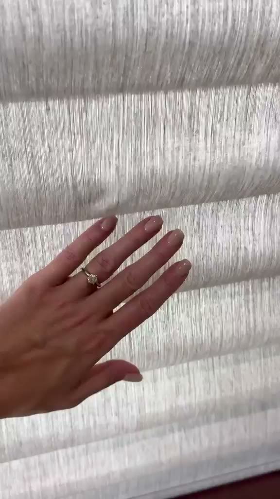 A hand brushing the textured sheer and solid bands of a layered shade